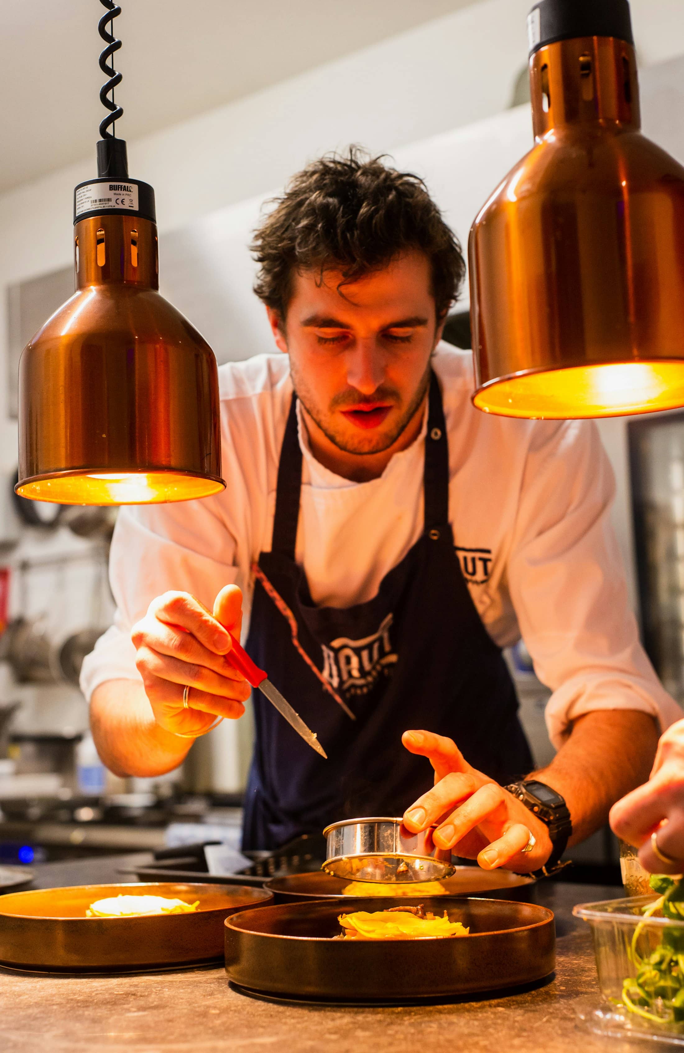 A chef plating food under copper pendant lamps