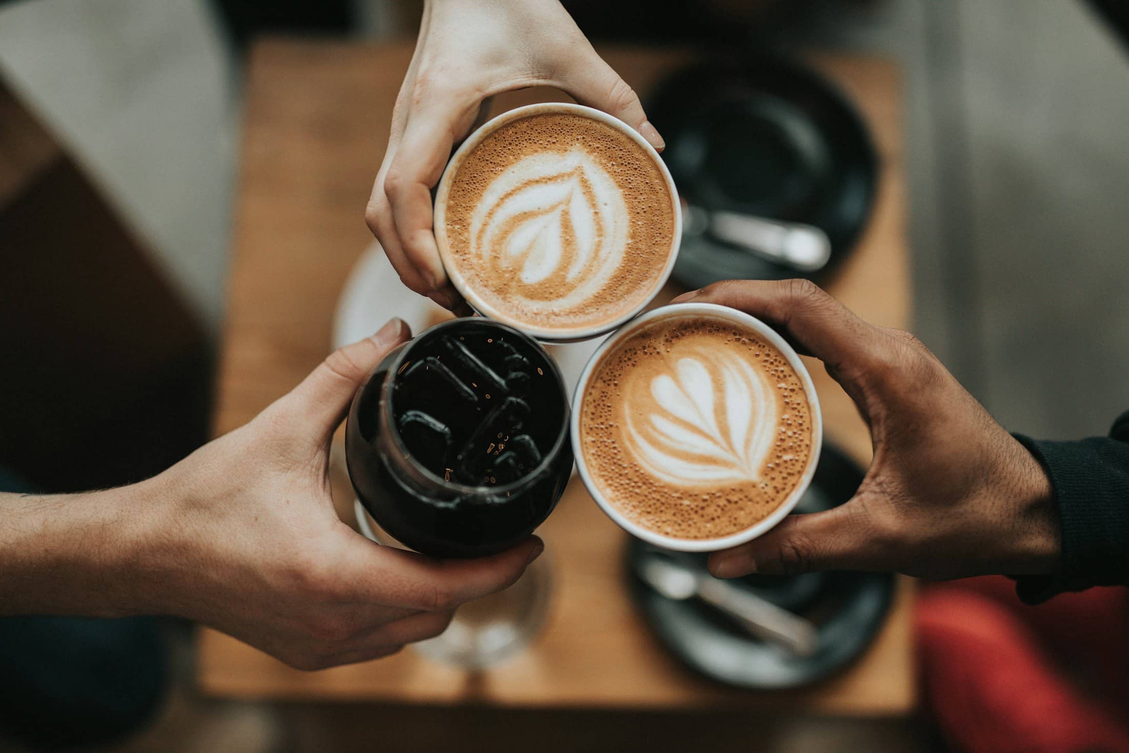 Two people raising cups of coffee with latte art across a table